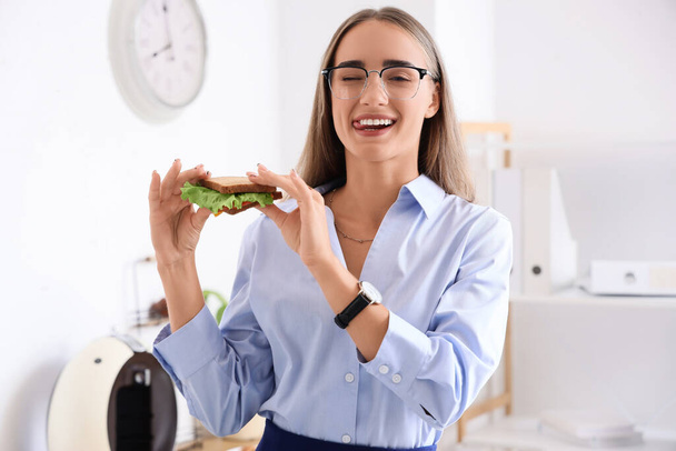 Bonita jovem empresária comendo saboroso sanduíche no escritório - Foto, Imagem