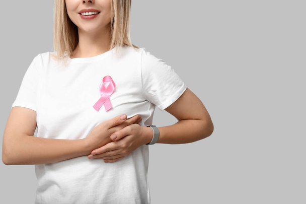 Young woman with pink ribbon on grey background.  Breast cancer awareness concept - Photo, Image