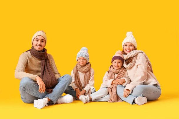 Familia feliz en ropa de invierno sentado sobre fondo amarillo - Foto, imagen