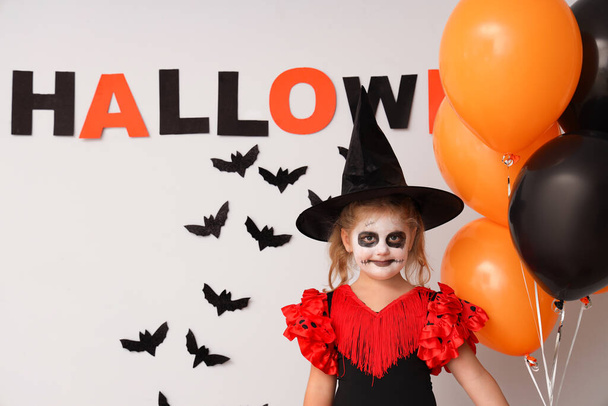 Little girl dressed for Halloween as witch with balloons and decor near light wall - Photo, Image