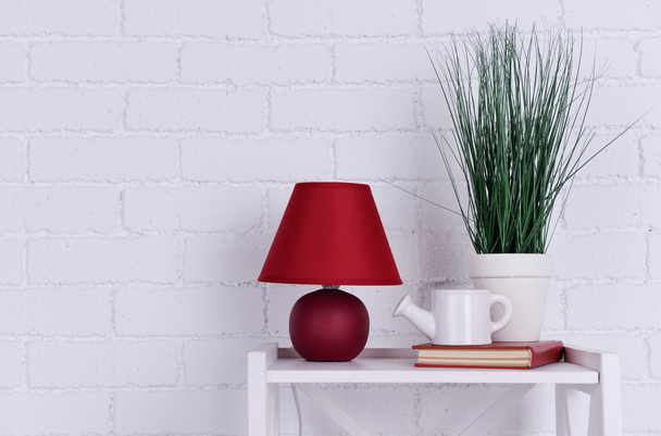 Interior design with lamp, plant, ceramic watering pot and book on tabletop on white brick wall background - Valokuva, kuva