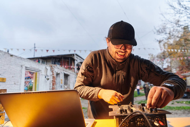 A young man is entertaining a group of friends in the backyard of his house, becoming their DJ and playing music in a casual outdoor gathering.  - Foto, imagen