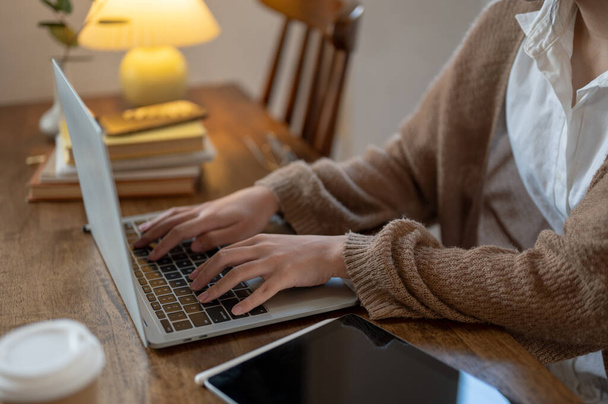 Laptop bilgisayarında çalışan, klavyede yazan, kahve dükkanında uzaktan çalışan rahat örülü bir kazak giymiş bir kadının yan görüntüsü.. - Fotoğraf, Görsel