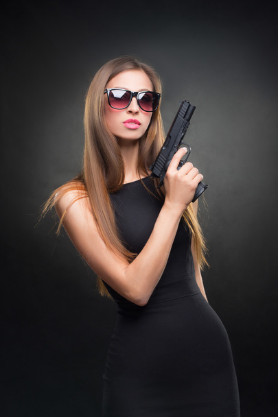 menina em um vestido preto e óculos de sol segurando uma arma
 - Foto, Imagem