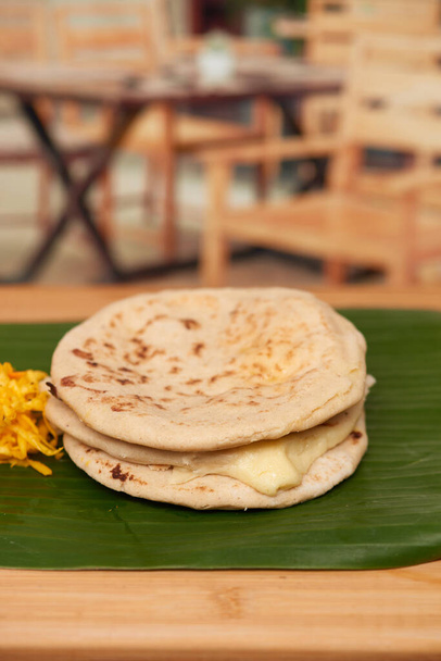 A captivating photo of authentic Salvadoran pupusas, featuring a cheesy filling and culinary artistry, set in a restaurant-style ambiance on a wooden surface accentuated by a leaf - Photo, Image