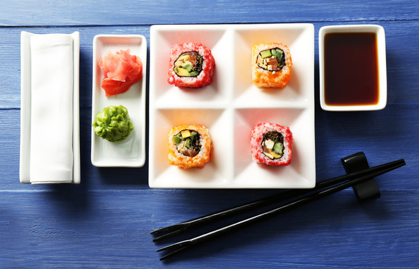 Sushi rolls on plate, soy sauce and chopsticks on color wooden background - Фото, изображение