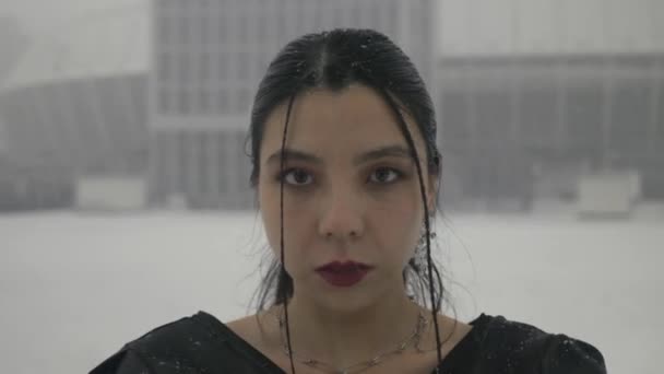 Muotokuva aasialaisesta naisesta katselemassa kameraa nauttimassa vapauden elinvoimaisuudesta lumisateen aikana, lähikuva. Nainen mustassa valossa kesävaatteet taustaa vasten luminen kaupunki - Materiaali, video