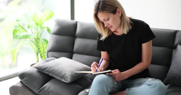 Γυναίκα χέρια γράφοντας σημειώσεις στο ημερολόγιο στον καναπέ στο σπίτι. Καταχωρήσεις στο προσωπικό ημερολόγιο και προγραμματισμός για μελλοντική προς υλοποίηση εργασία - Πλάνα, βίντεο