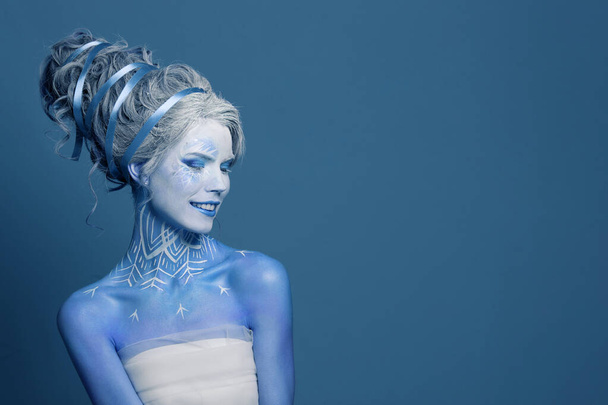 Cool zima królowa kobieta z białym makijażem kreatywnym, idealna fryzura i śnieg na niebieskim tle. Karnawał lub Halloween party makijaż. Zimowa wróżka, portret studenta mody - Zdjęcie, obraz
