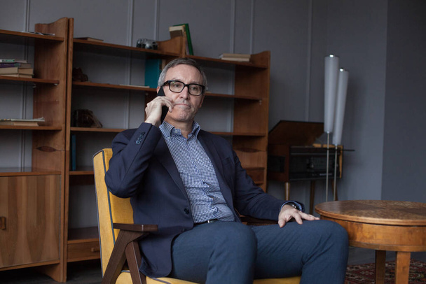 Uomo d'affari serio in giacca e cravatta e occhiali che parla sul cellulare su sfondo grigio - Foto, immagini