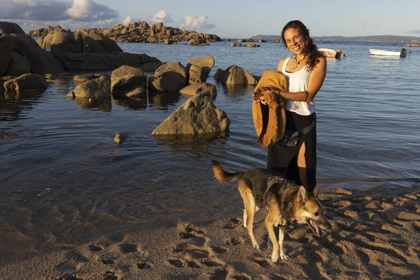 晴れた夏の日にガリシア・スペインの水に隣接する犬とビーチでセクシーなヒスパニック女性 - 写真・画像