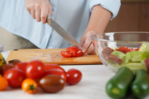 Žena v procesu výroby zeleninového salátu. Detailní záběr rukou krájejících rajčata na dřevěném stole - Fotografie, Obrázek