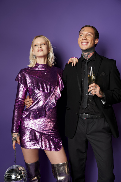 Kerstmis, dromerig koppel in feestkleding met glas champagne en discobal op paars - Foto, afbeelding