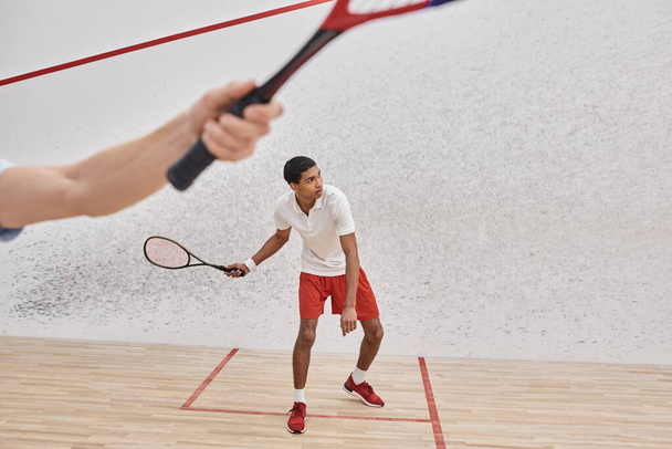 african american man in sportswear playing with friend inside of squash court, blurred foreground - Foto, Imagem