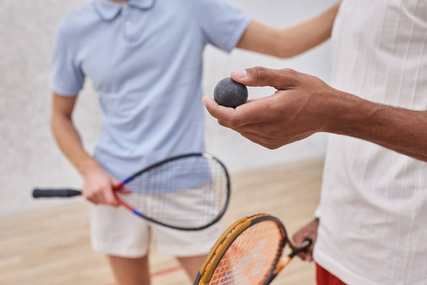 oříznutý pohled na afrického Američana držícího squashový míček v blízkosti přítele uvnitř dvora, hráče - Fotografie, Obrázek