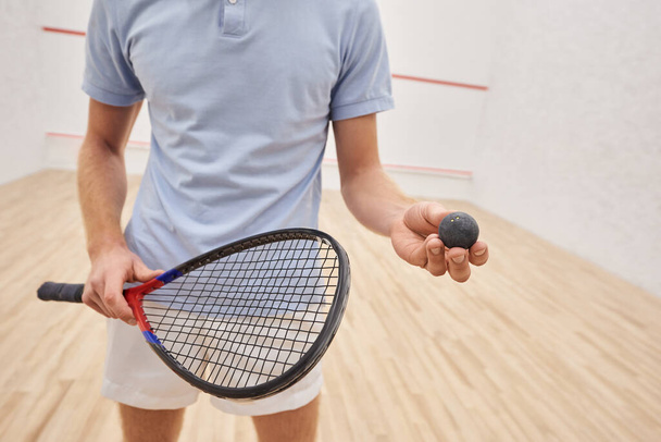 bijgesneden beeld van de mens in sportkleding met squash bal en racket en staande in de rechtbank - Foto, afbeelding