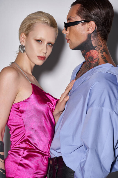 blonde woman in pink dress posing with tattooed boyfriend in sunglasses on grey, New Year party - Photo, Image