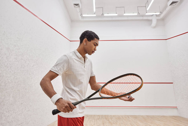 african american man in active wear holding squash ball and racquet while playing inside of court - Foto, Bild