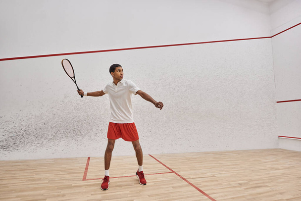 atlético afroamericano hombre celebración squash raqueta y saltar mientras juega juego en la corte - Foto, Imagen