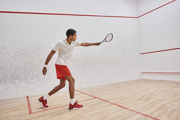 side view, athletic african american man in active wear holding racquet while playing squash - Foto, Imagem