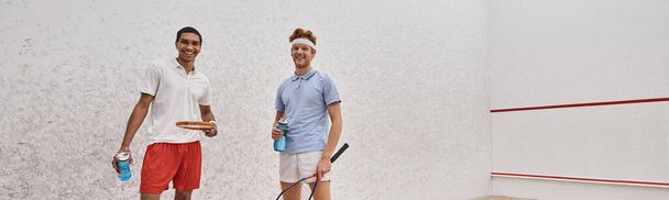 deportistas interracial alegre con raquetas de calabaza y botellas con agua de pie en la corte, pancarta - Foto, Imagen