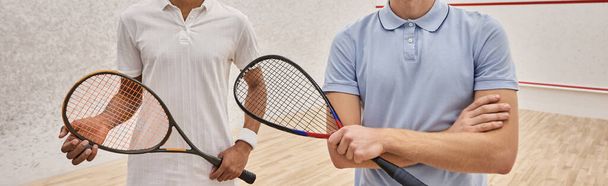 amigo macho interracial recortado de pie junto con raquetas de squash en la corte, pancarta - Foto, imagen