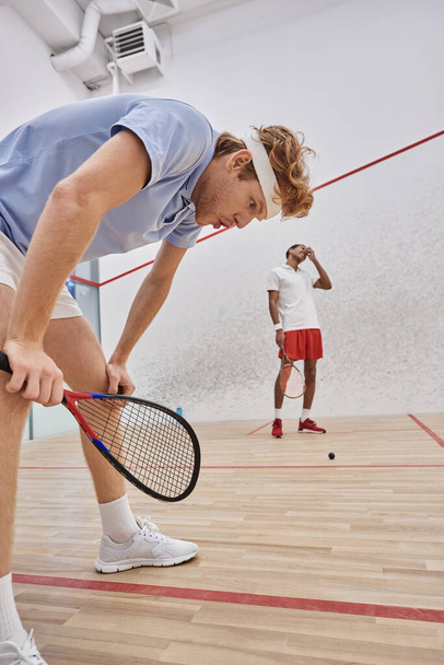 zmęczeni wielokulturowymi graczami w odzieży sportowej ciężko oddychający po grze w squasha w sądzie - Zdjęcie, obraz