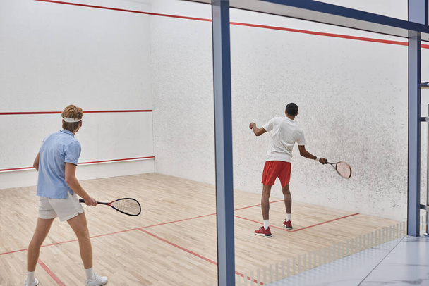 multicultural players in sportswear playing squash together inside of court, motivation and sport - Fotografie, Obrázek
