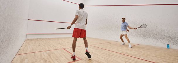 hombres atléticos interracial en ropa deportiva jugando squash juntos dentro de la corte, bandera de motivación - Foto, imagen