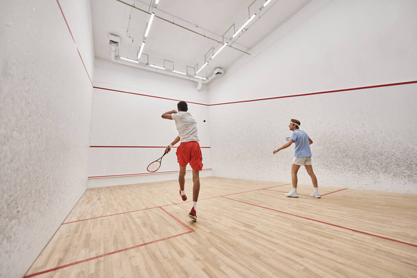 interracial players in sportswear playing squash together inside of court, fitness and motivation - Photo, Image