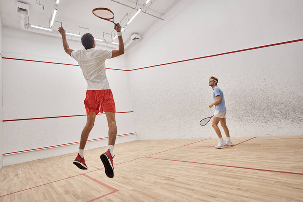 interracial players in sportswear jumping and playing squash inside court, challenge and motivation - Photo, Image