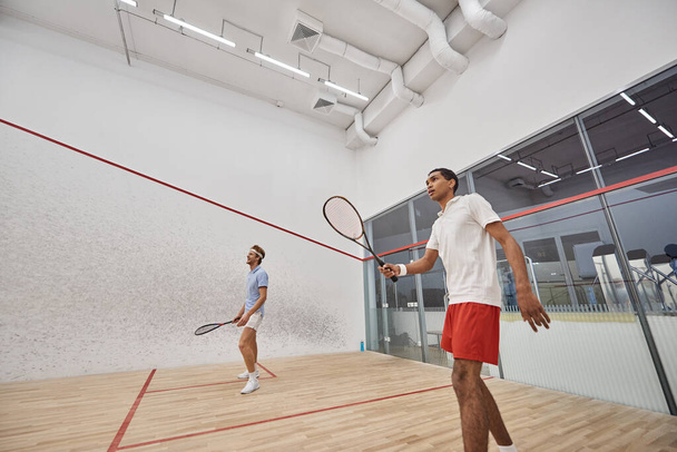 young and interracial men in sportswear playing squash inside of court, challenge and motivation - Foto, immagini