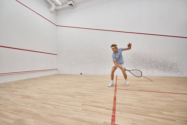 nuori ja aktiivinen punapää mies urheiluvaatteet pelaa squash sisällä tuomioistuin, haaste ja motivaatio - Valokuva, kuva