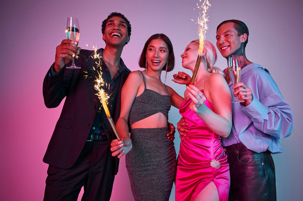 Celebración de Año Nuevo, alegres cuatro amigos multiétnicos sosteniendo bengalas y champán en rosa púrpura - Foto, imagen