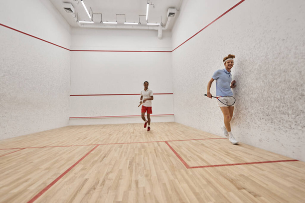 joueurs interraciaux dynamiques jouant au squash ensemble à l'intérieur du court, défi et motivation - Photo, image