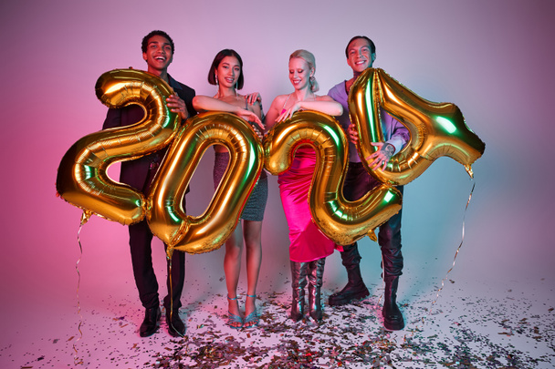 Nieuwjaarsfeest, vrolijke interraciale vrienden in feestelijke kleding houden ballonnen met 2024 nummers - Foto, afbeelding