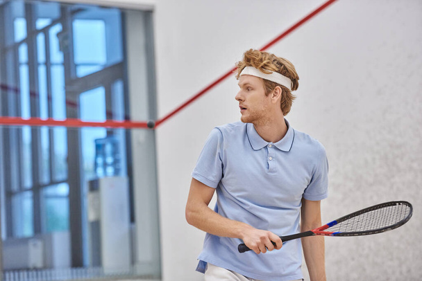 athletic redhead sportsman holding racquet while playing squash inside of court, training shot - Fotoğraf, Görsel