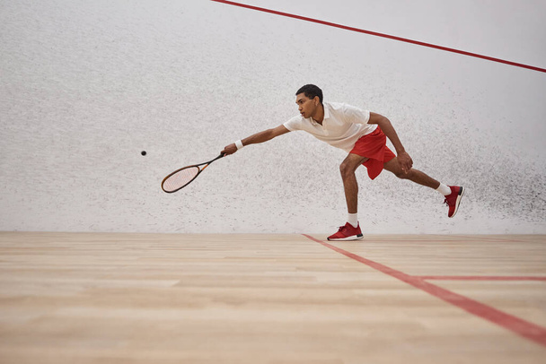 african american sportsman in red shorts holding racquet and playing squash inside of court, sport - Foto, Bild