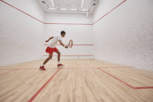 african american sportsman in sports shorts holding racquet while playing squash inside of court - Foto, Bild