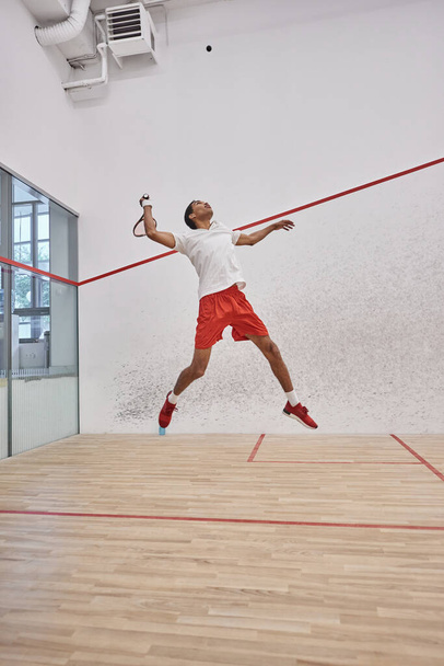 motion shot, energetic african american player holding racquet while jumping and playing squash - Фото, изображение