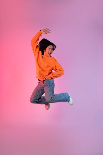 Image of a young Asian person dancing on a neon colored background - Photo, Image