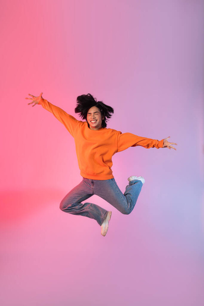 Image of a young Asian person dancing on a neon colored background - Photo, Image