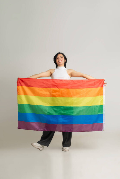 白い背景に自信を持って虹の旗を掲げているアジアのゲイ男性のイメージ - 写真・画像