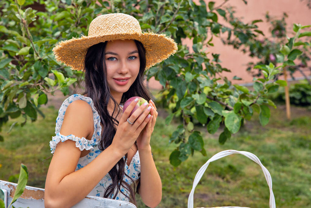 果樹園に座ってリンゴのクローズアップを保持している美しい若いブルネット白人女性. - 写真・画像