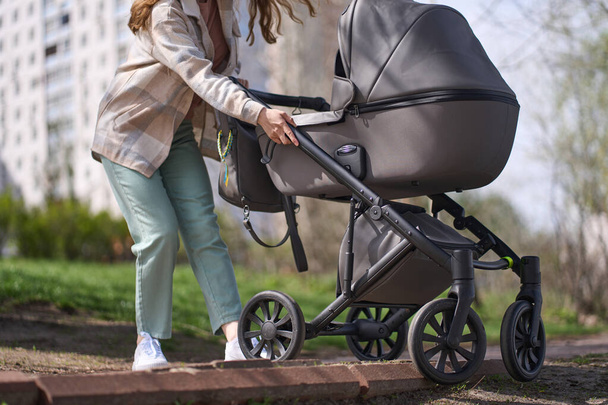 Крупним планом молода кавказька жінка мати, навряд чи тягне дитячу коляску зі своєю новонародженою дитиною вгору по сходах або тротуарі під час прогулянки в природному парку - Фото, зображення