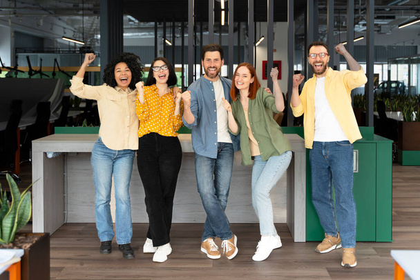 Successful team of diverse business partners colleagues clenching fists from excitement, smiling looking at camera, standing in modern corporate office interior. People. Teamwork. Career - Photo, Image