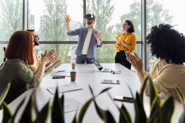 Натхненний кавказьким молодим чоловіком в окулярах VR, грає в онлайн ігри віртуальної реальності під час командної підготовки в сучасному офісному інтер'єрі. Люди. Кар'єра. Професійне та особисте зростання. - Фото, зображення