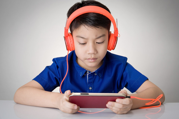 アジアの少年ウェア ヘッドフォンと携帯電話を再生 - 写真・画像