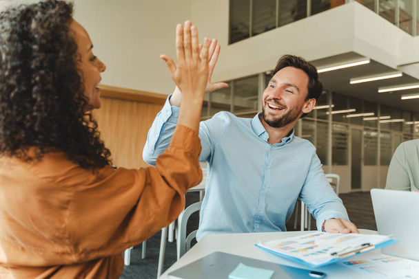 Portrait of happy business people, workers, colleagues giving high five celebration success sitting in modern office. Startup, career, successful business concept  - Photo, Image