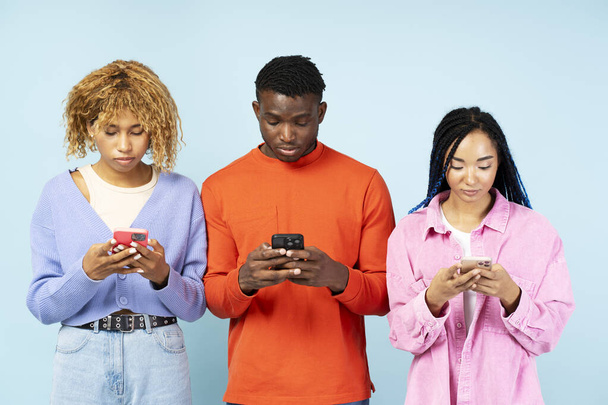 Gruppe verschiedener junger afroamerikanischer Studenten in lässigem farbigem Outfit mit Handy, SMS und Online-Shopping isoliert auf blauem Hintergrund. Technologiekonzept - Foto, Bild